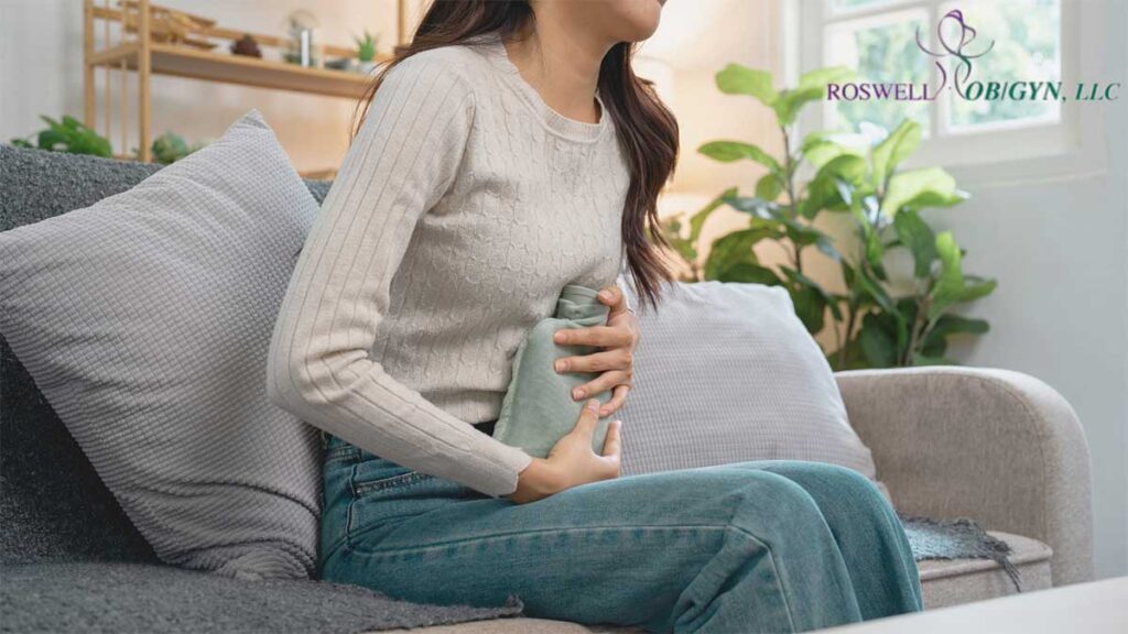 A woman suffering from menstrual pain, holding a warm compress to her abdomen for relief.